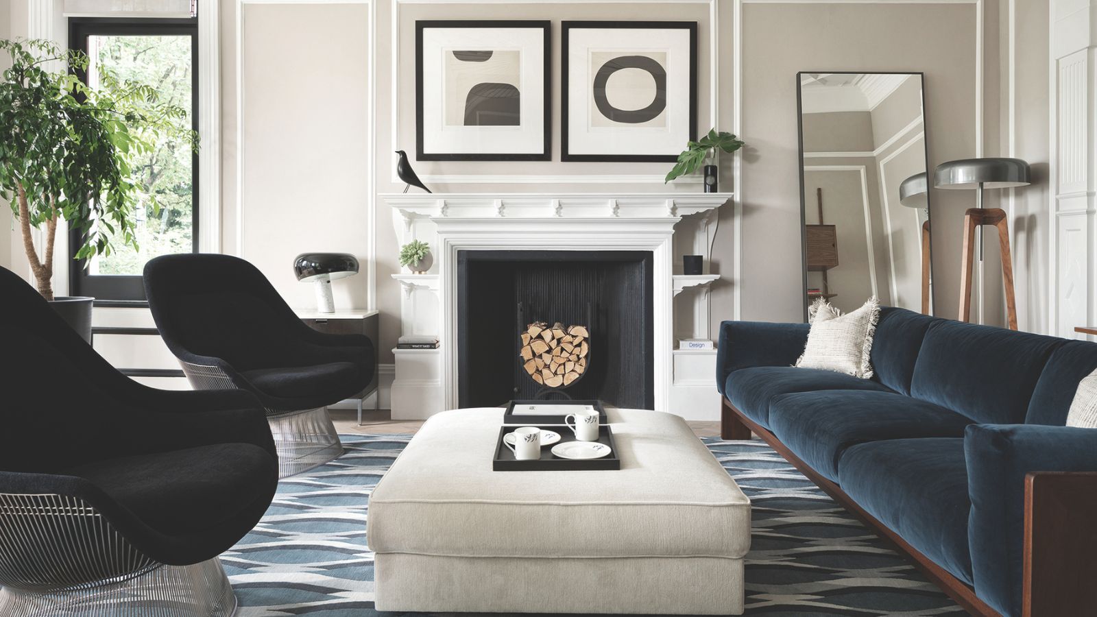 Minimalist living room with monochrome scheme, velvet sofa, black armchairs, wall art, fireplace with wood and cream ottoman