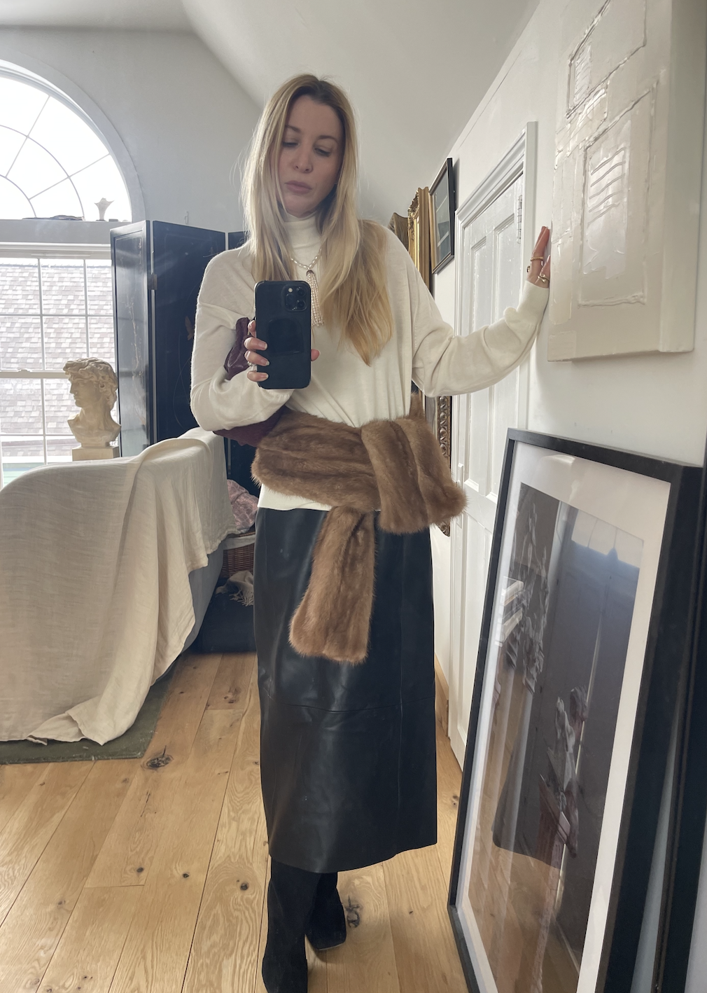 Kerry Pieri wearing a black leather pencil skirt, white thin knit turtleneck, and brown fur scarf as a belt