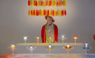 Artist wearing red and yellow standing behind glass lighting
