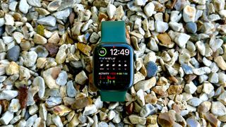 En Apple Watch 7 med ett grönt armband ligger på en bädd av småstenar.