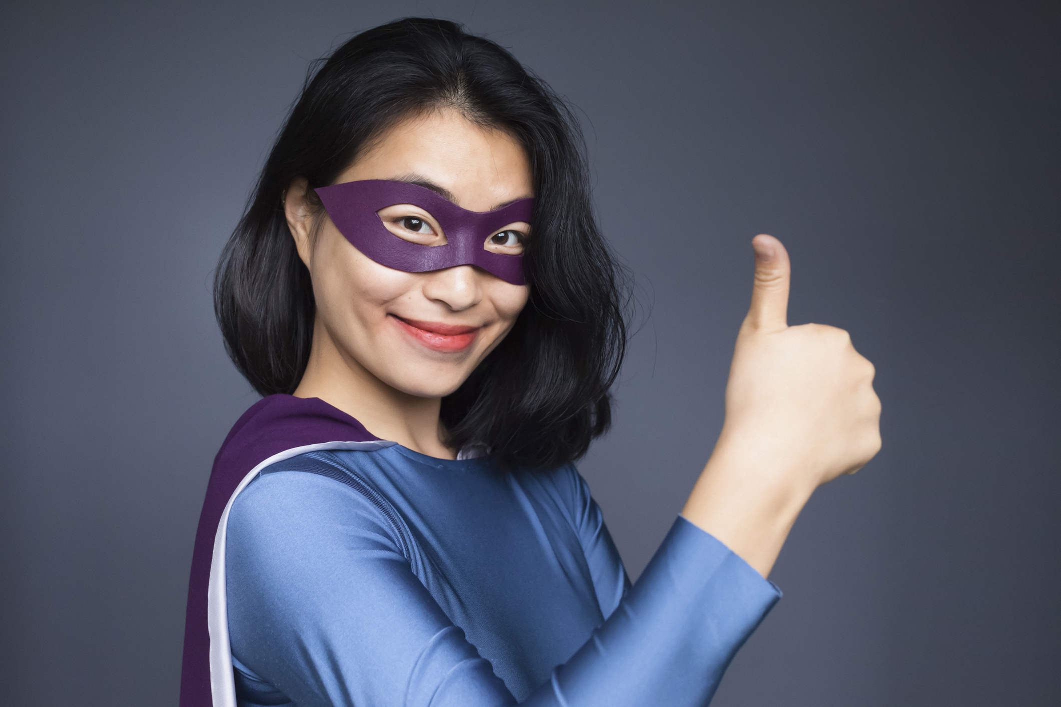 Portrait of confident female superhero gesturing thumbs up against gray background