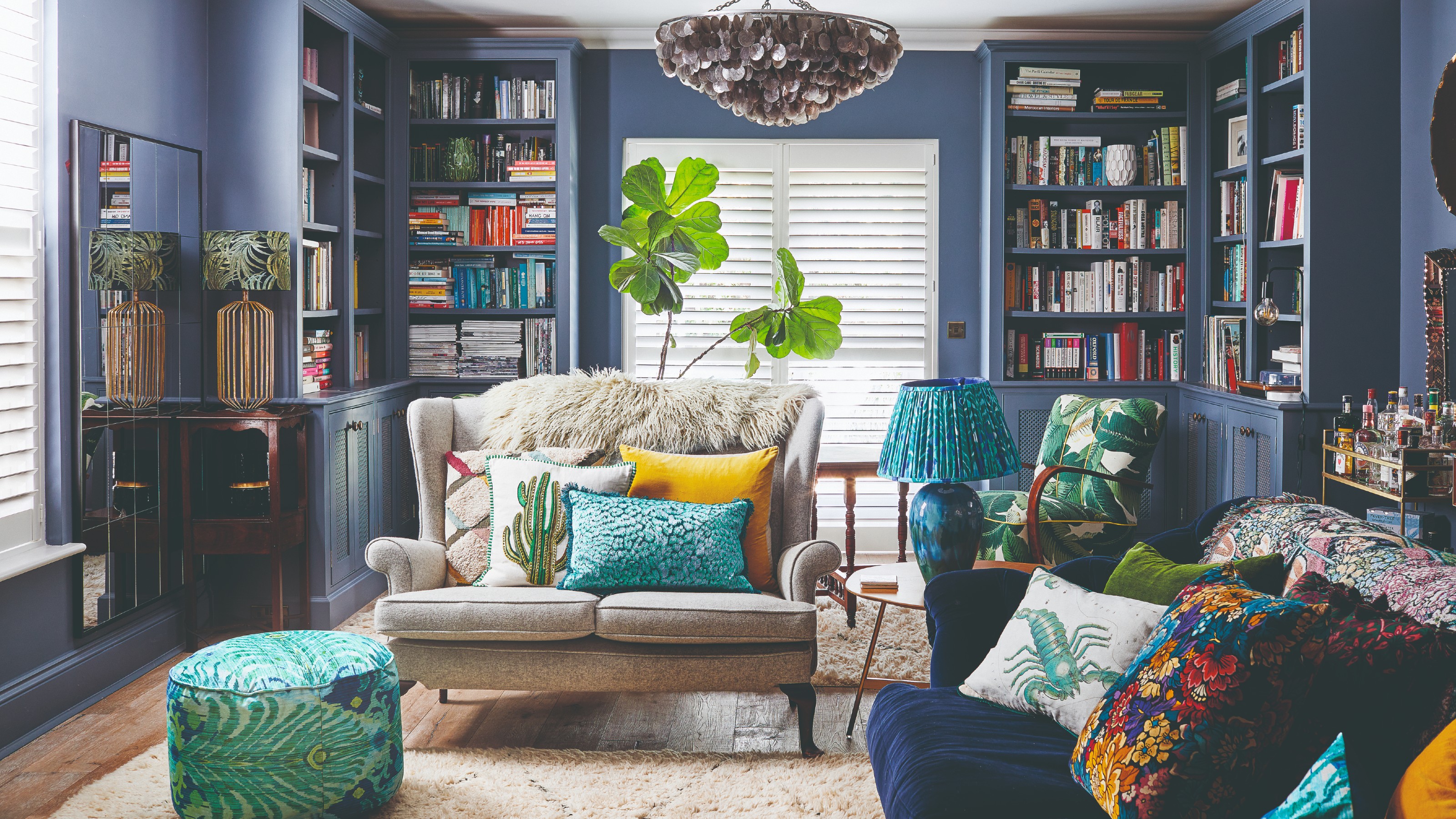 A blue living room with matching bookcases along the walls and colourful cushions on a blue velvet sofa and beige loveseat