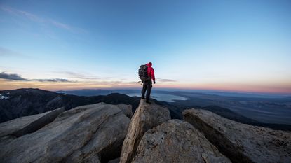 A hiker stands on top of a mountain looking at the view.