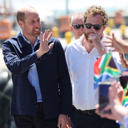 Prince William waving at a crowd waving flags