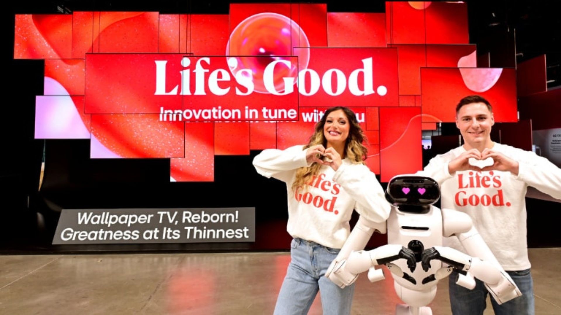 LG CES show with the LG Cloid home robot doing a heart symbol with its hands. A person stands either side of the Cloid