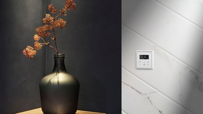 A white thermostat on a white wall , beside a sideboard with a grey vase with some dried flowers