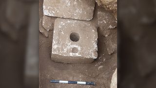 We see a stone block with a hole in the middle. It is surrounded by other stone blocks.