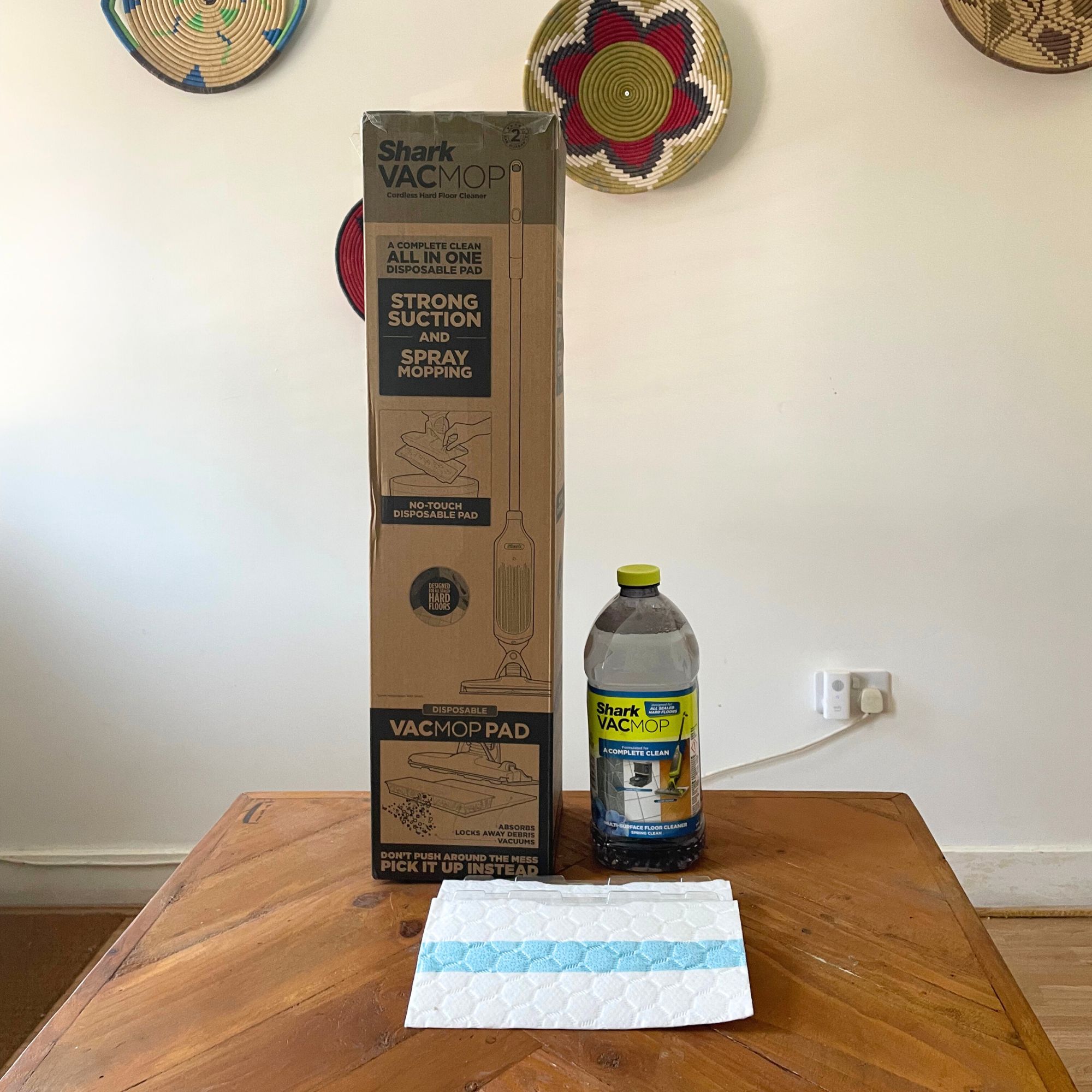 Shark VacMop box and accessories sitting on a wooden table in front of a white wall