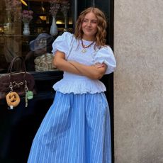 Influencer wears the Damon Madder white blouse with detachable sleeves with a blue striped skirt and mule trainers.