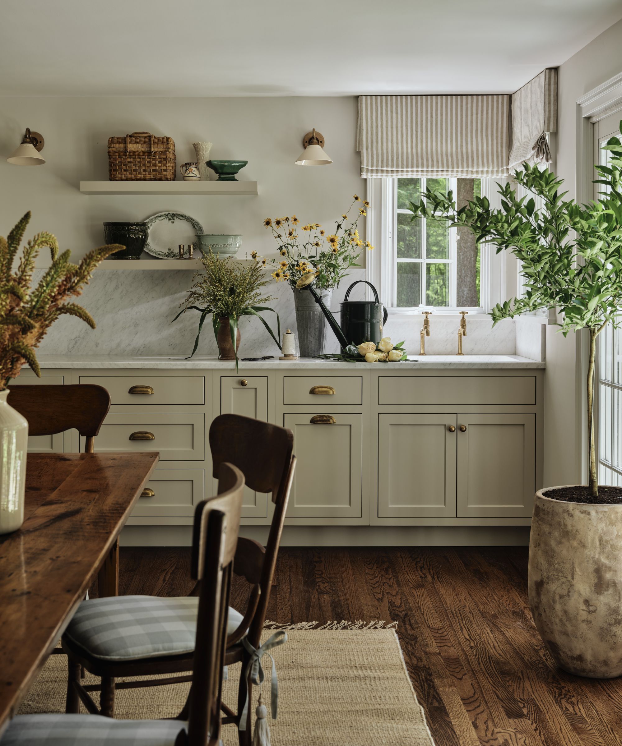 a warm neutral english country style kitchen with open shelving and marble counters. A rustic farmhouse table and chairs sit in the middle of the room