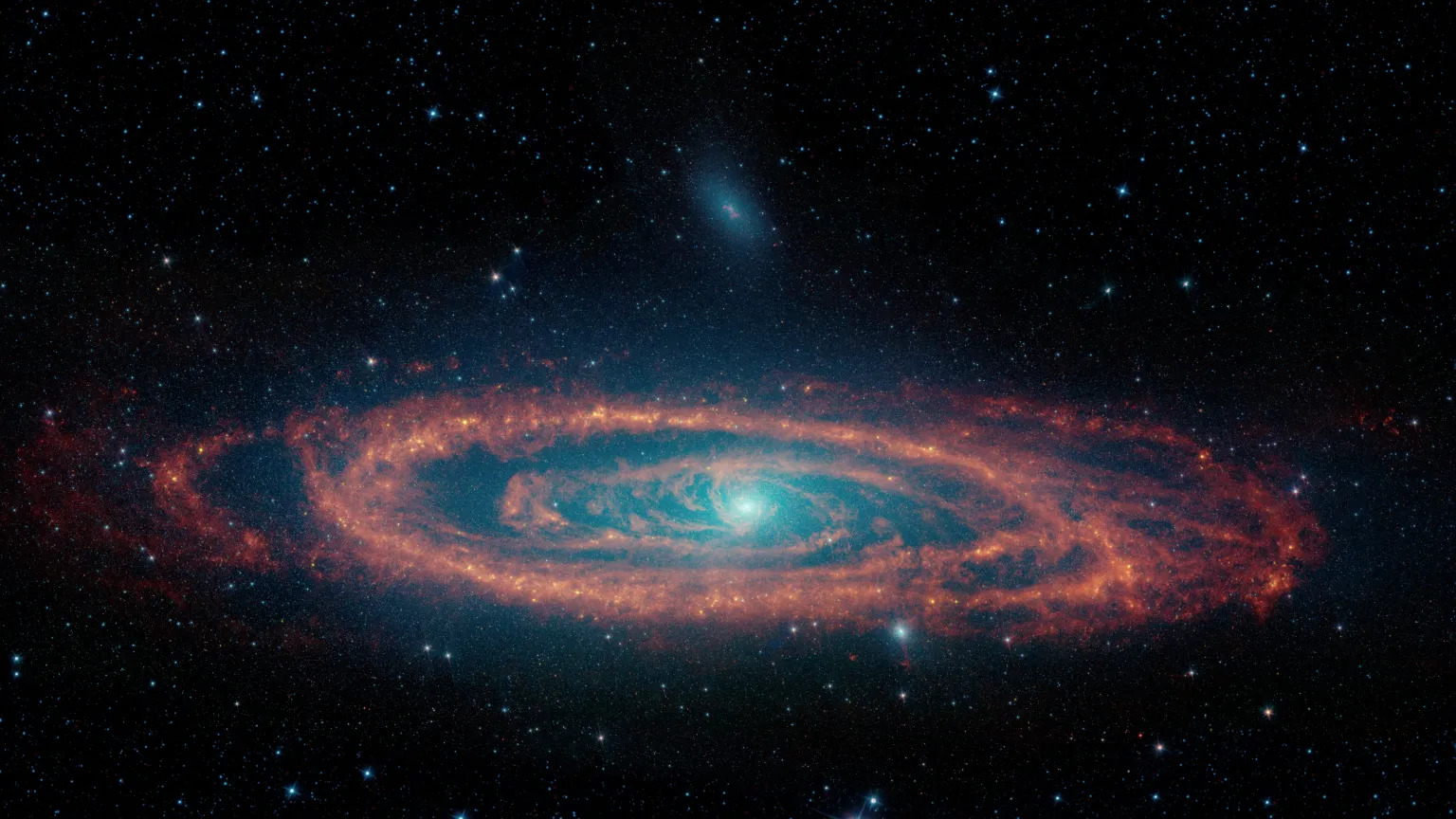 An image of a galaxy against the backdrop of space. It has a blueish center, is seen kind of edge-on  and has reddish disks around the central region.