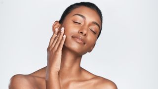 Woman with clear skin touching her face on a grey background