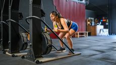 Woman using cardio machine in the gym. She is holding two green handles connected to cords and is bent over