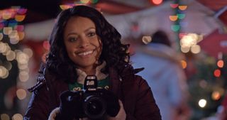 Kat Graham holds a camera in a Christmas setting