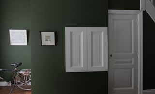 Dark grey walls with picture frames and a white door. In the right corner of the image is an adult bicycle.