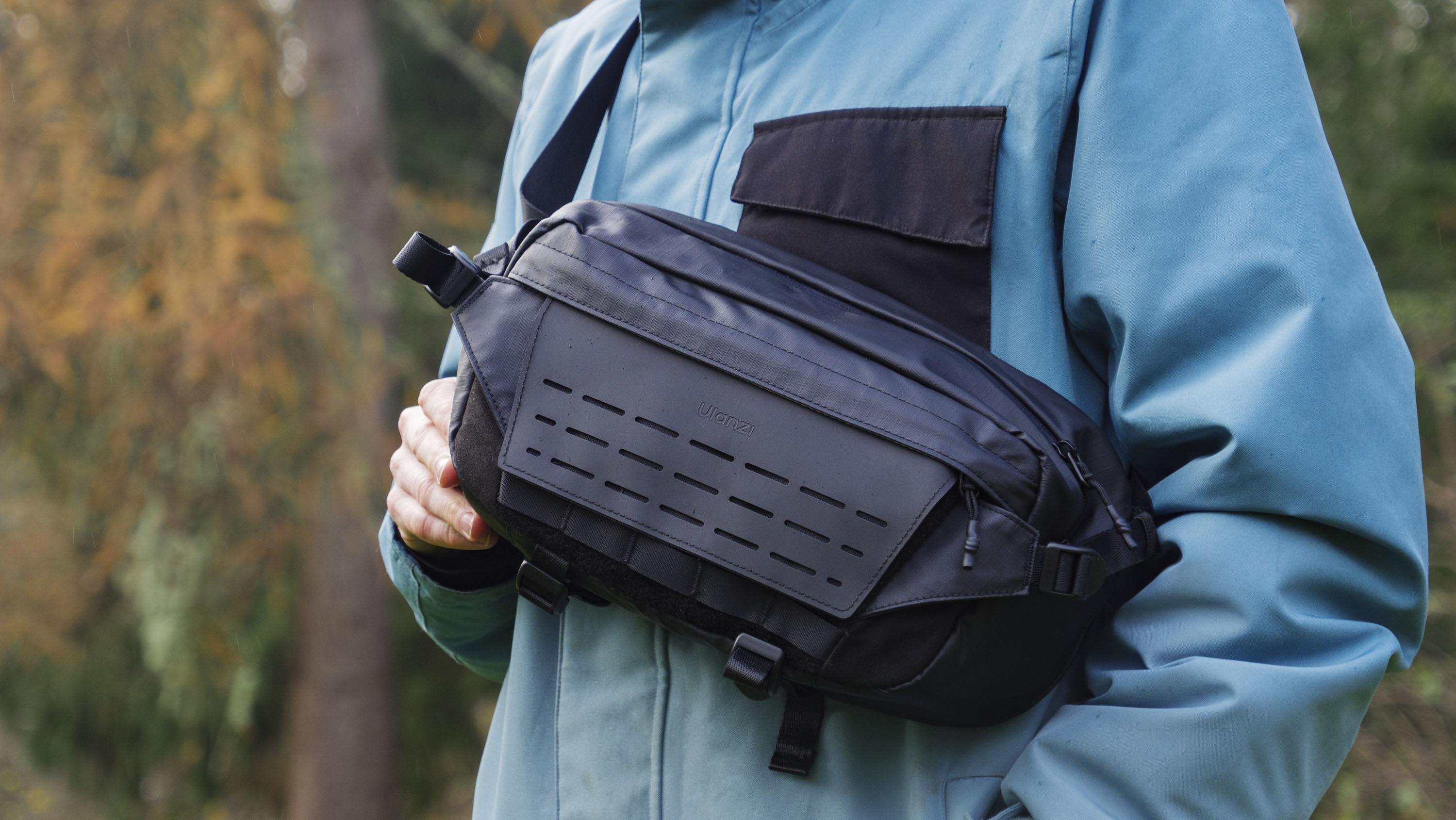 Man wearing a blue jacket outside with a Ulanzi Camera Sling Bag over his shoulder and resting on his midriff