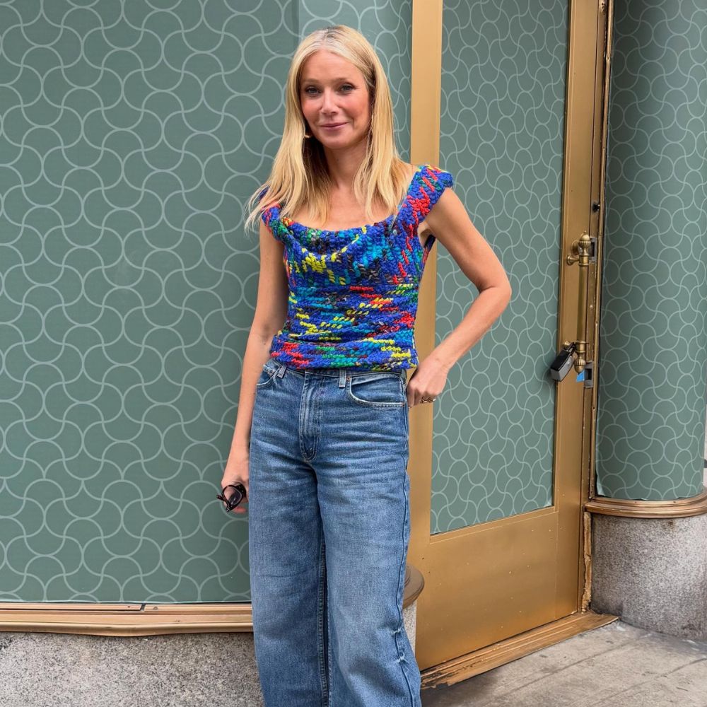 Gwyneth Paltrow poses for a photo wearing blue wide-leg cropped jeans with red heels and a blue top.