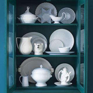 blue storage cabinet with white cups tea pots and plates