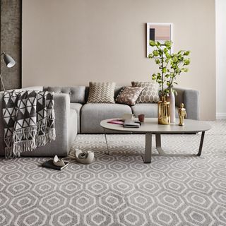 grey living room ideas, grey living room with grey patterned carpet, grey sofa, grey walls, artwork, L shaped sofa, side table, graphic print cushions