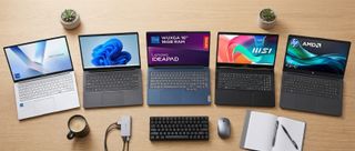 Five business laptops arcing around a clean desk in a brightly lit office
