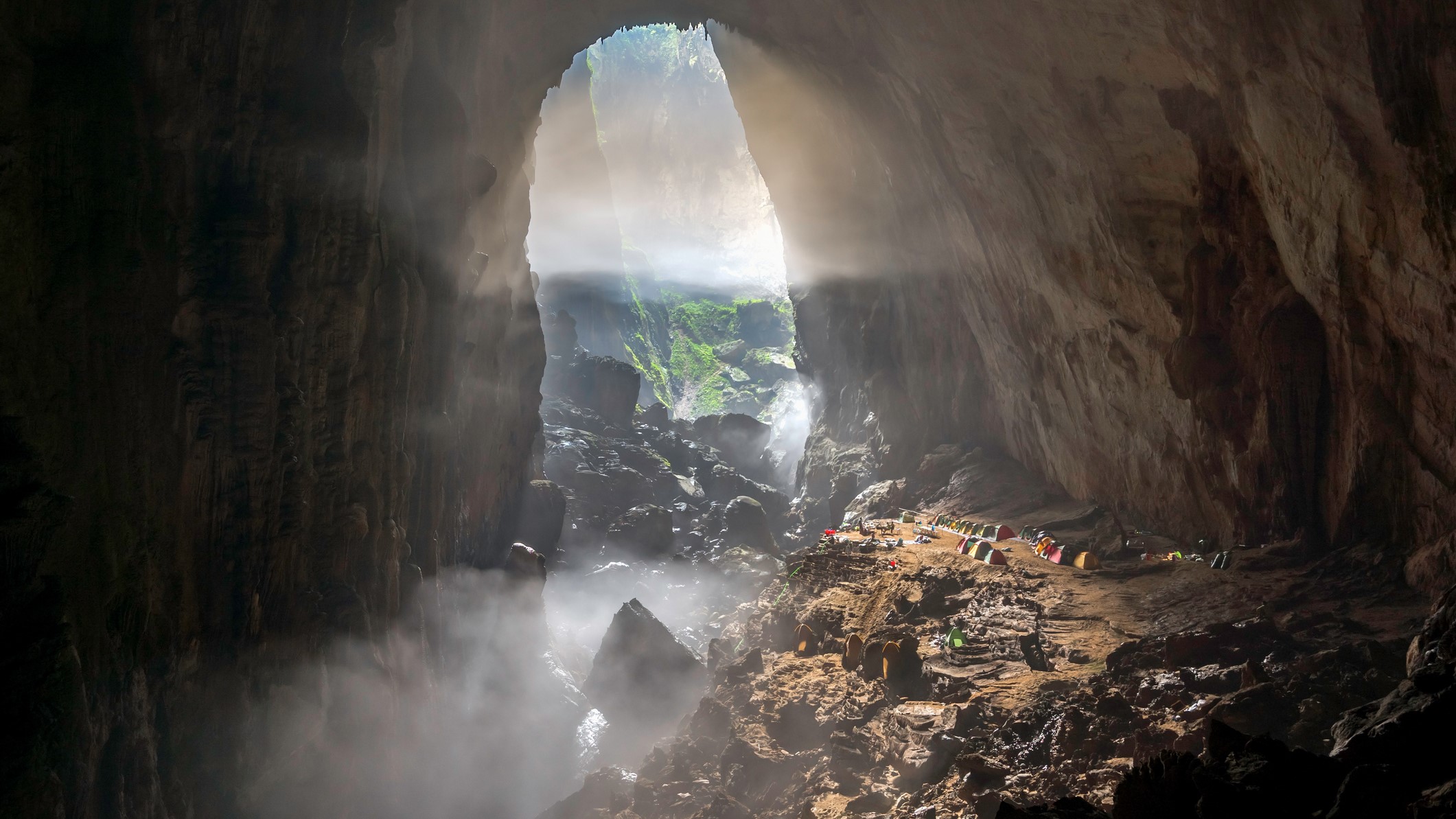 Inside a large cave with light filtering in through the entrance. Clouds are forming within the cave.