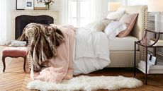 Eclectic bedroom with herringbone wooden floors, antique furniture, and a studded upholstered bed that is layered with pink-on-white and white-on-pink bedding