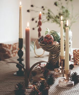 A table with a gingham tablecloth decorated with candlesticks, pinecones and a bowl filled with baubles