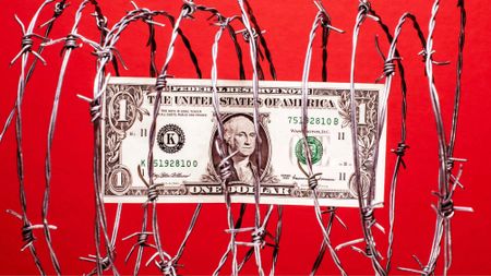 $1 US dollar bill inside coil of steel barbed wire, red background