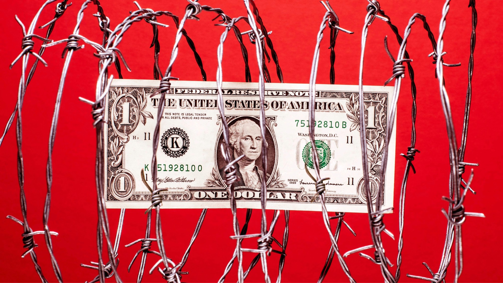 $1 US dollar bill inside coil of steel barbed wire, red background