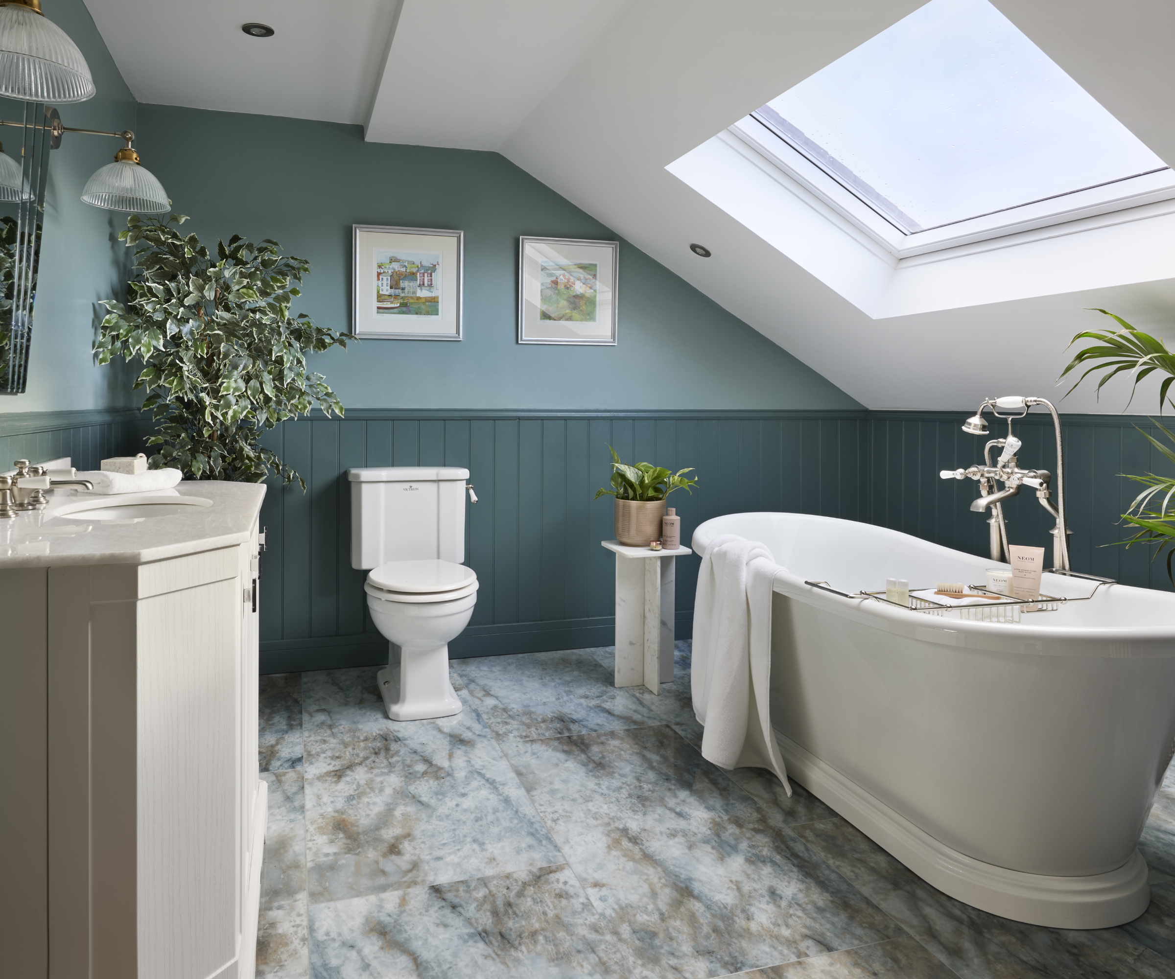 bathroom with white freestanding bath with brushed nickel tapware, blue marble floor tiles, blue wall panelling and skylight above bath