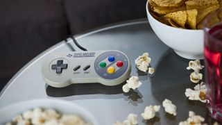 A vintage Nintendo SNES controller photographed on a glass table, surrounded by bowls of snacks