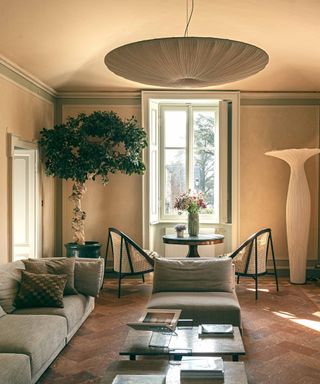 A neutral living room with a gray sofa, bright window, and hanging pendant light