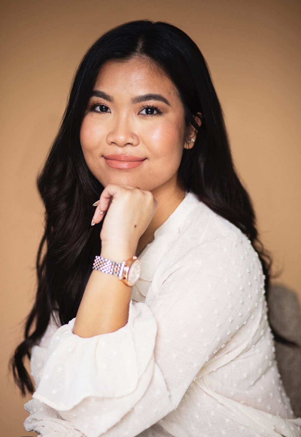 A woman, Queenie Nguyen, wearing a white dotted blouse with long dark hair poses for a headshot.