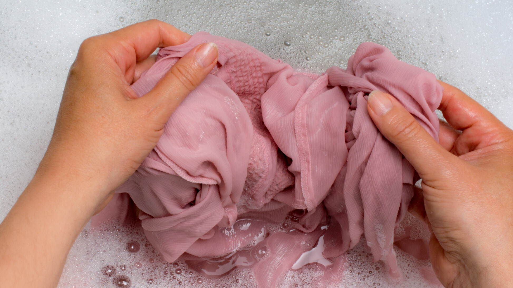 Handwashing a pink silk pillowcase in soapy water