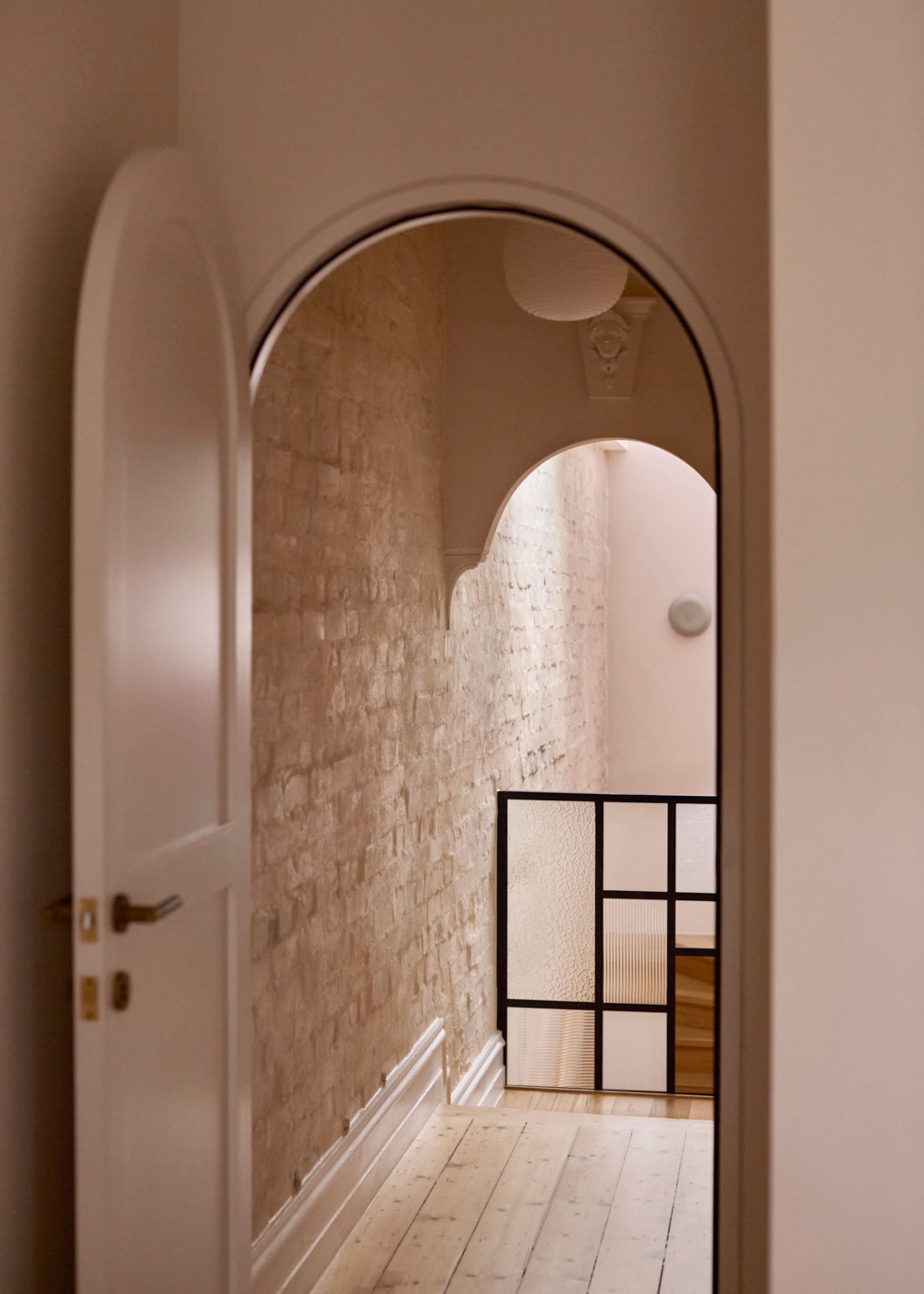 An arched pale pink door leading to a glass barrier and a wood staircase