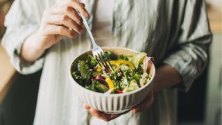 Bowl of dressed salad, woman putting fork into bowl