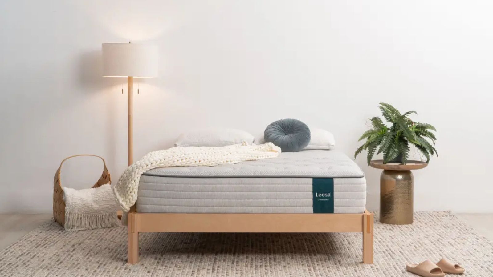 Cushions and a blanket on a Leesa mattress on a bed against a white wall.