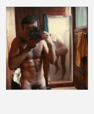 Naked man stood in the mirror holding a camera