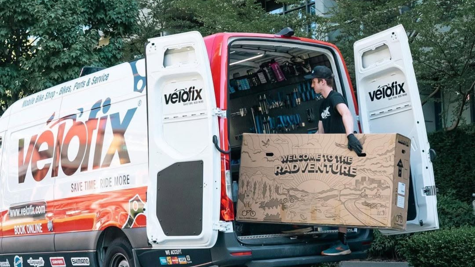 VeloFix technician carries a boxed bike into his mobile bike shop