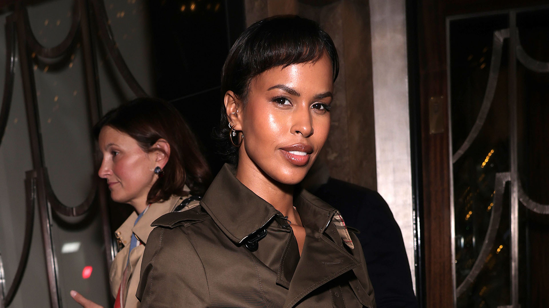 Sabrina Elba wearing a green trench coat, green pants, and plaid pumps