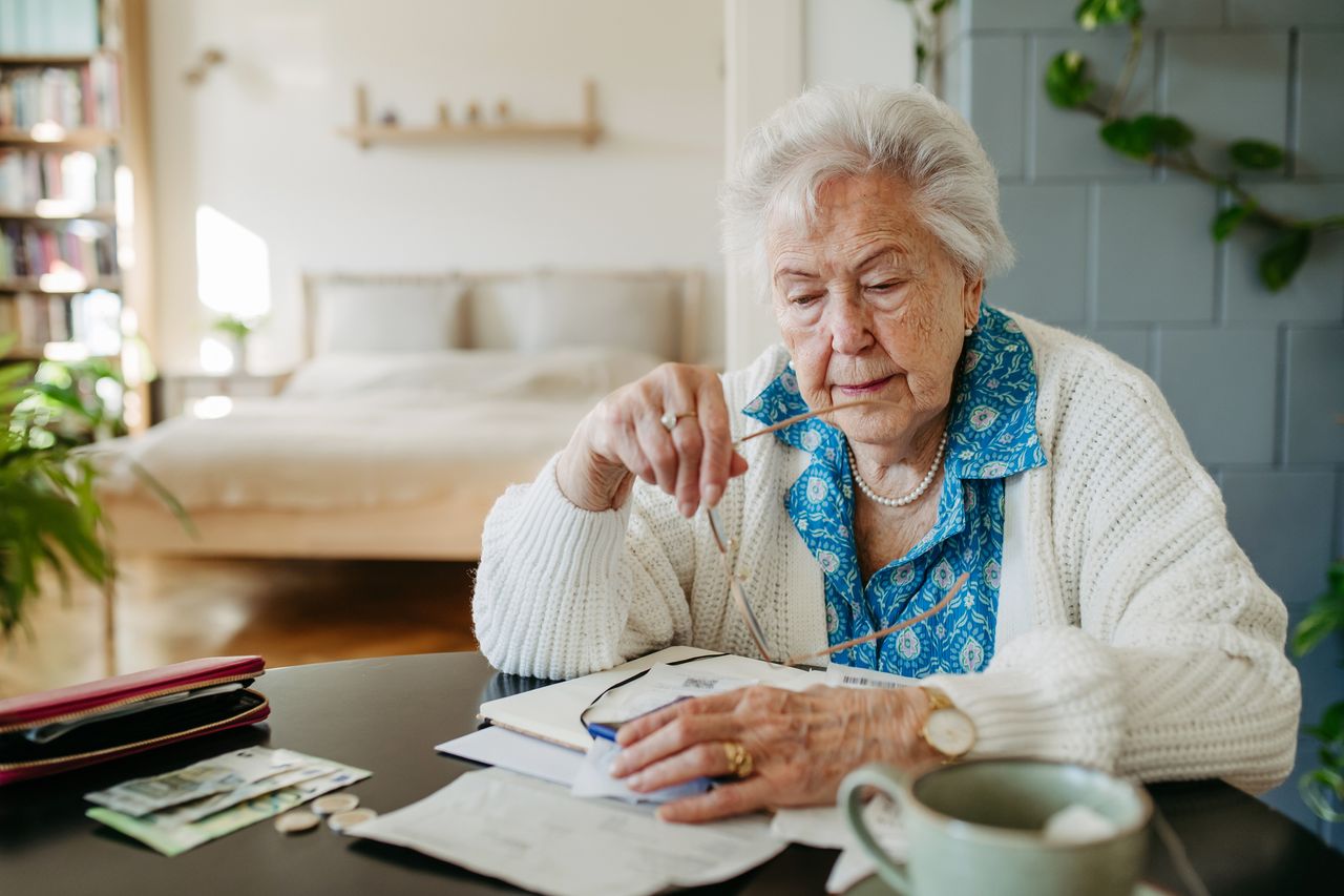 An older woman sits at a desk looking at financial documents.