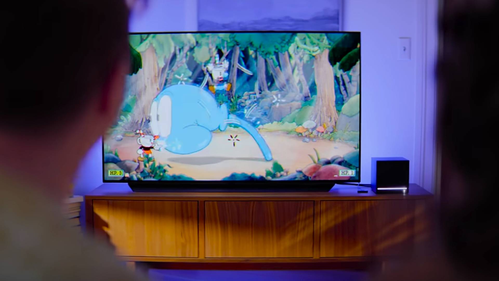 Steam Machine hooked up to TV with Cuphead on screen and two players sitting in front of camera.