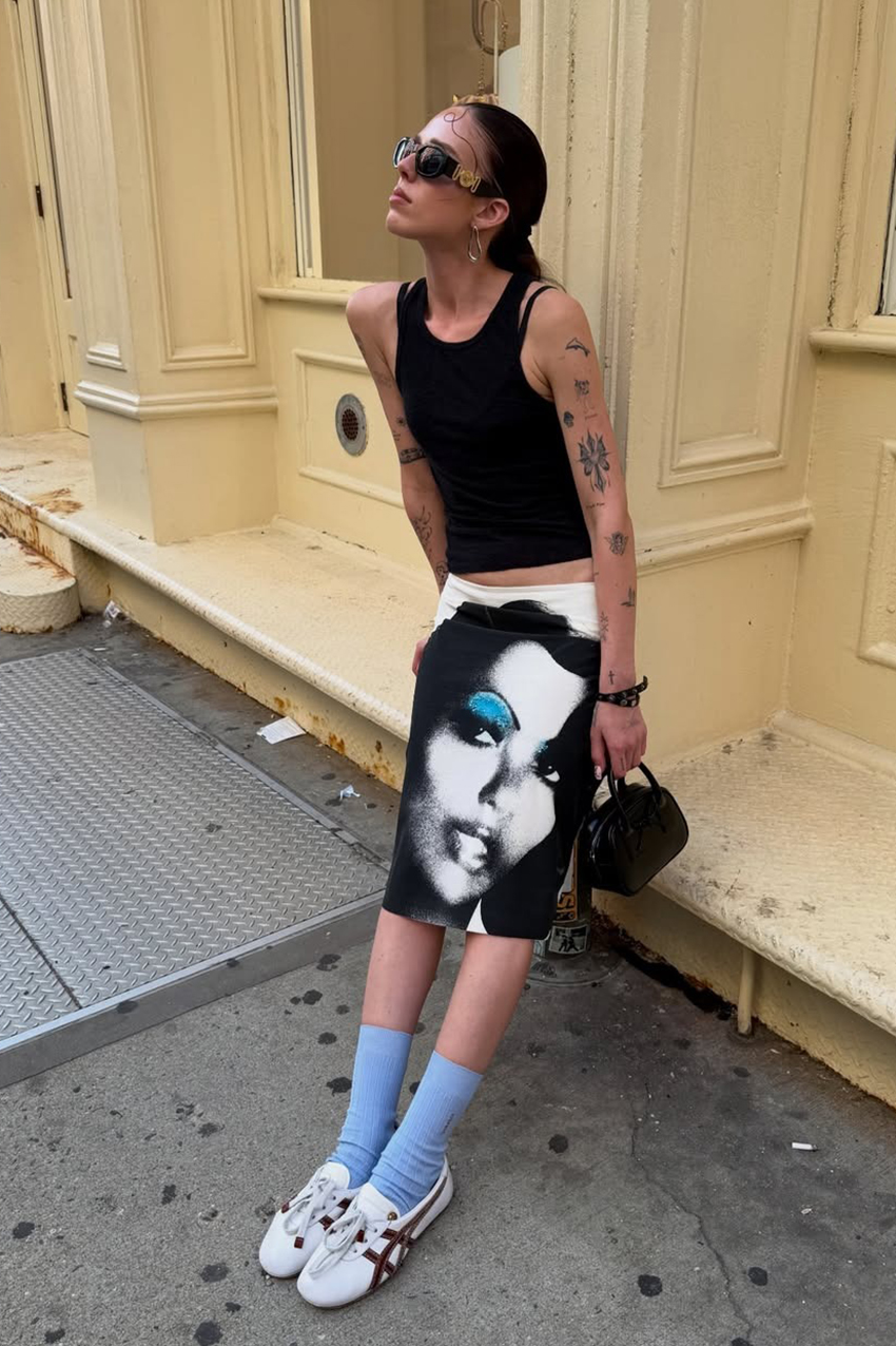 a woman wearing a black tank top, black skirt, blue socks, and white sneakers