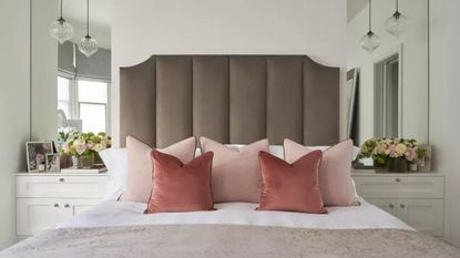 A grey headboard with pink pillows and two bedside mirrors 