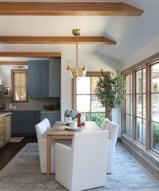 An open-plan kitchen and dining room with white upholstered chairs and wooden raftered ceilings