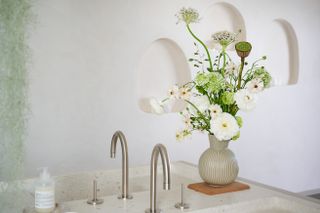 A glass vase filled with white flowers and foliage next to a kitchen sink