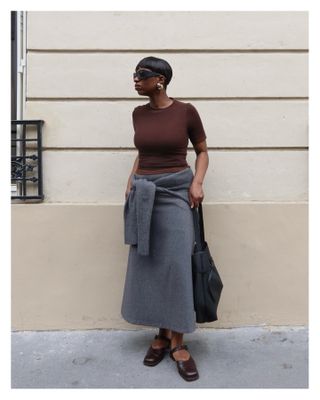 girl wearing a brown tee and grey skirt with flats