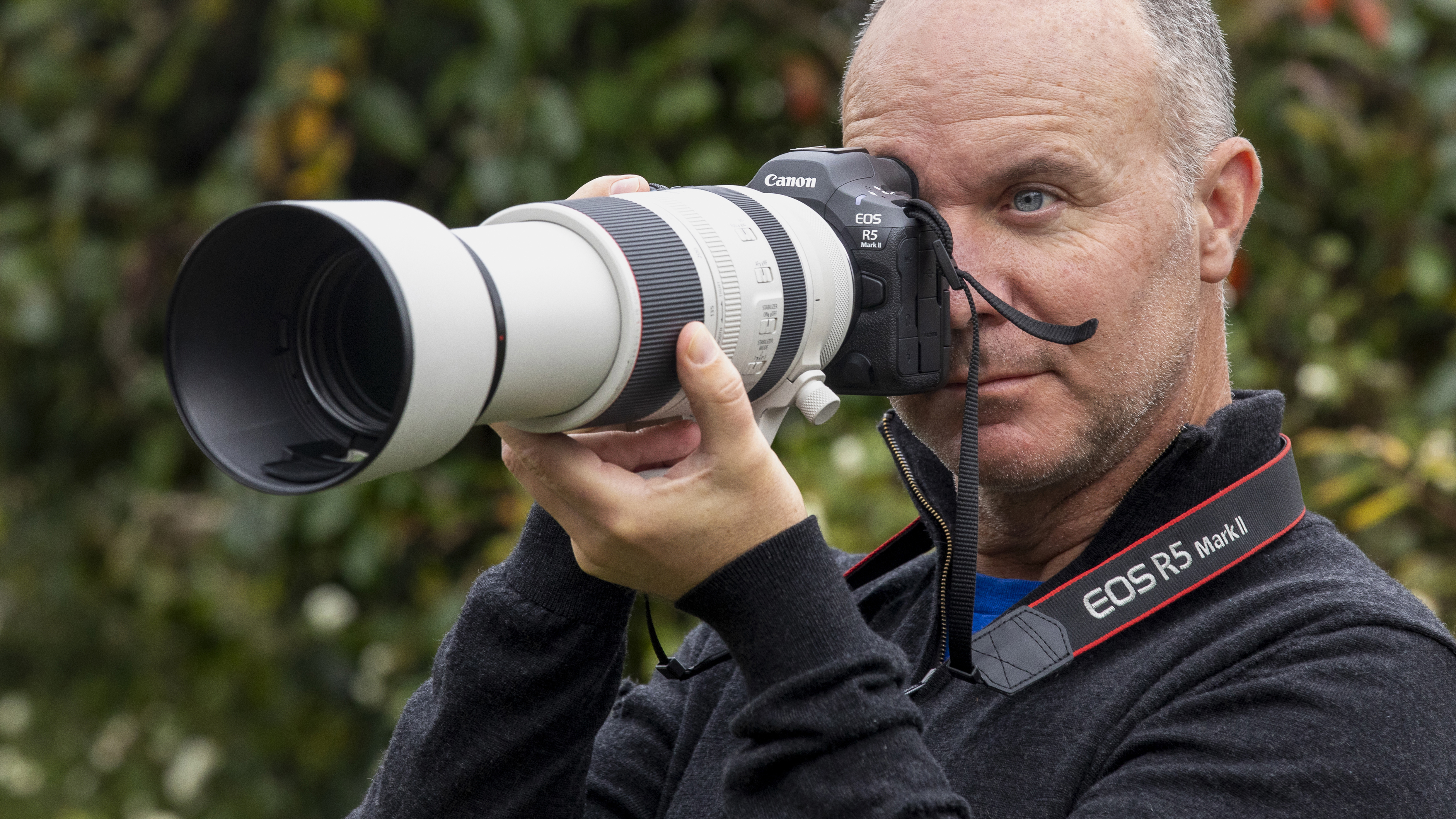Photographer using a Canon EOS R5 Mark II and RF 100-500mm lens with green foliage blurred behind