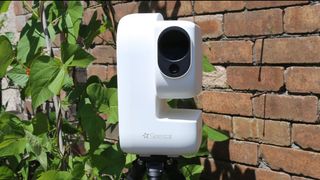 A ZWO Seestar S50 Pro against a brick background and green leaves.