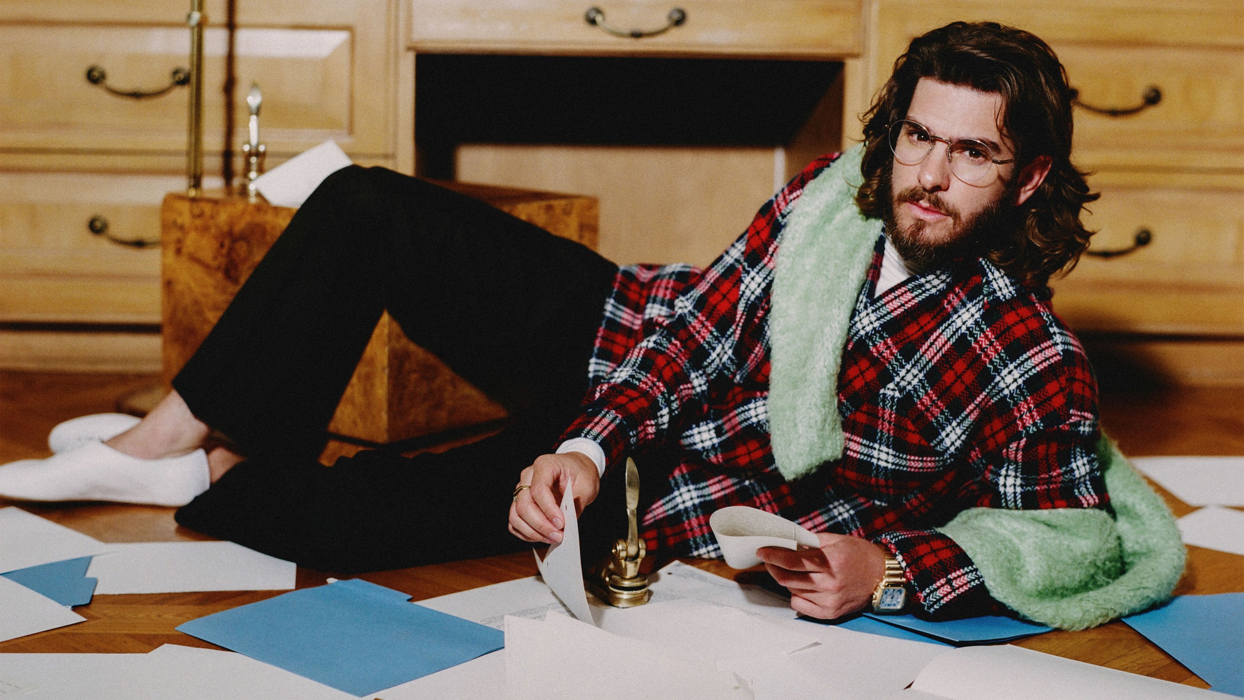 Andrew Garfield for Who What Wear's September cover, wearing a plaid button-down with a green sweater over his shoulders, black pants, and white shoes.